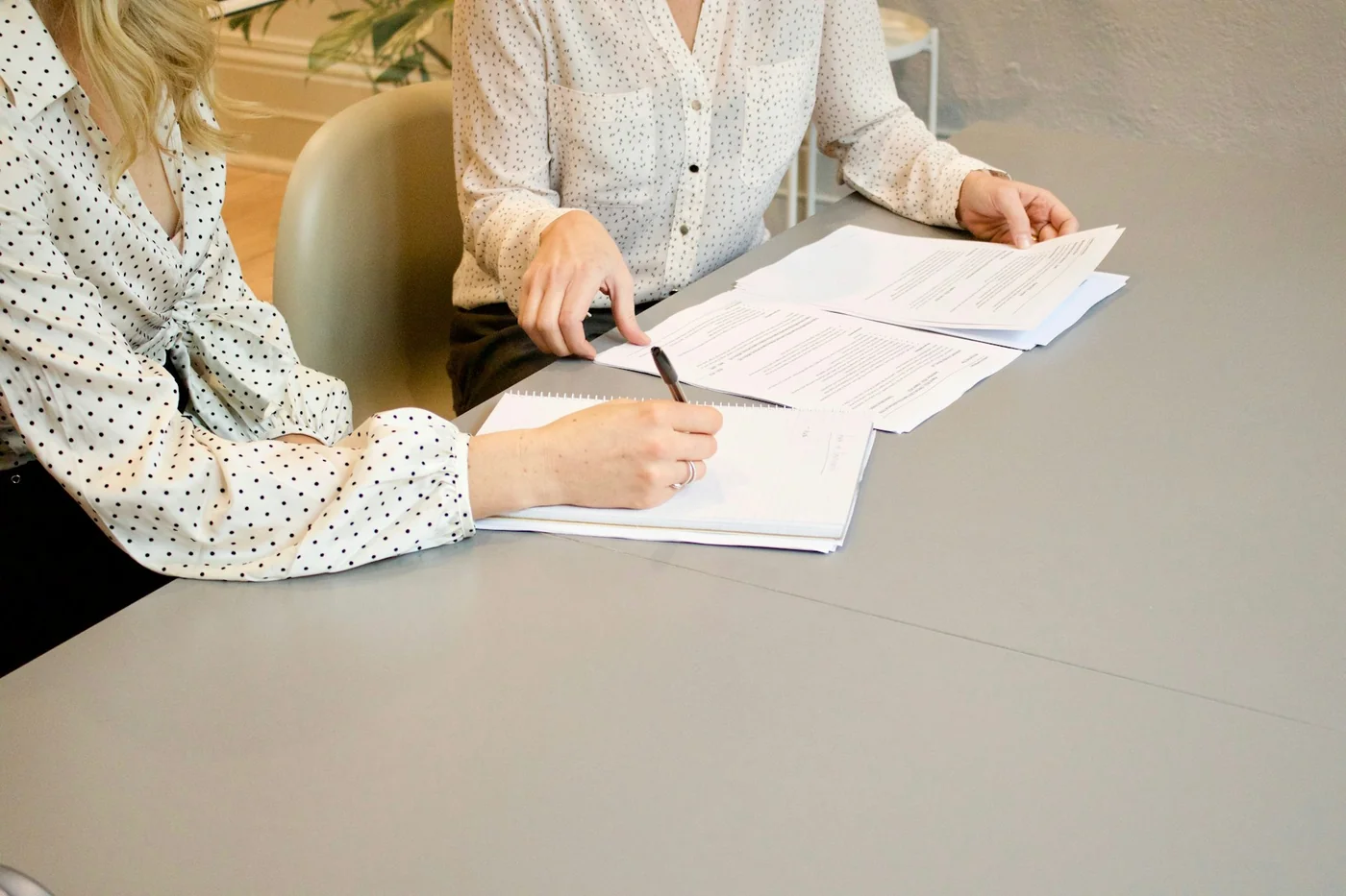 Duas pessoas conferindo e assinando documentos sobre uma mesa.